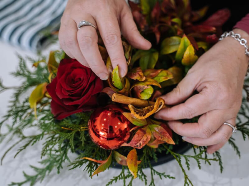 Overhead view of hands making a festive wreath of foliage and dried fruit